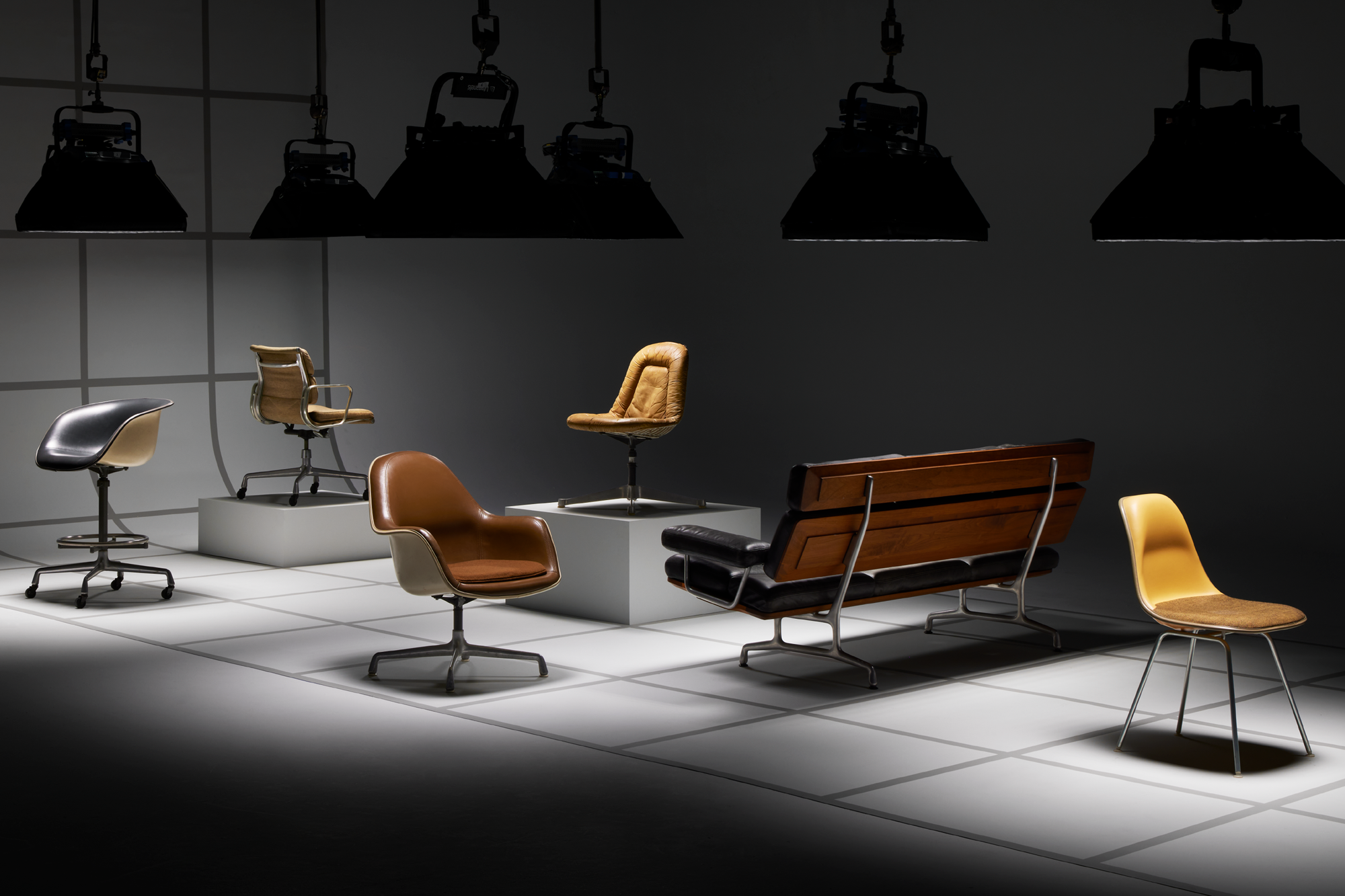 Several Eames chairs including the EC176 Loose Cushion Armchair and Eames Sofa in a setting with dramatic lighting.
