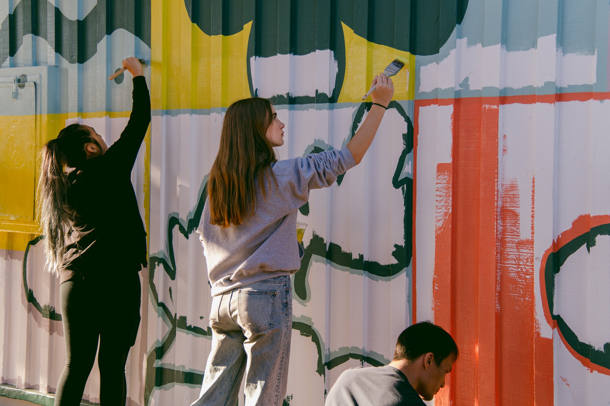 Two students painting a brightly colored mural for Project Color Corps.